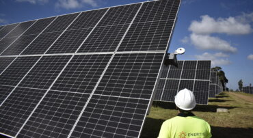 Engineer inspecting large solar panel array at a utility‑scale solar farm under a clear blue sky, highlighting renewable energy technology and solar power operations.
